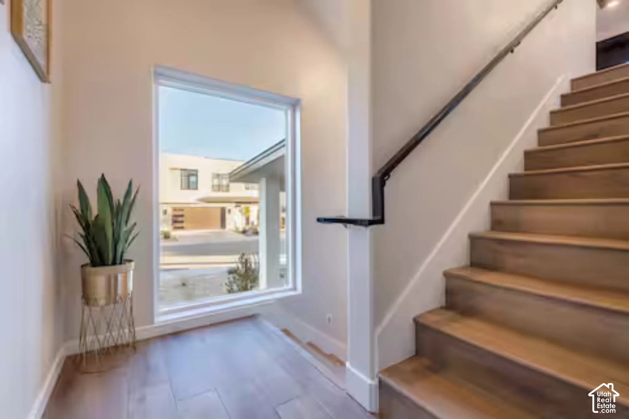 Wood-finish flooring, staircase with wood treads, black metal handrail, and a large window