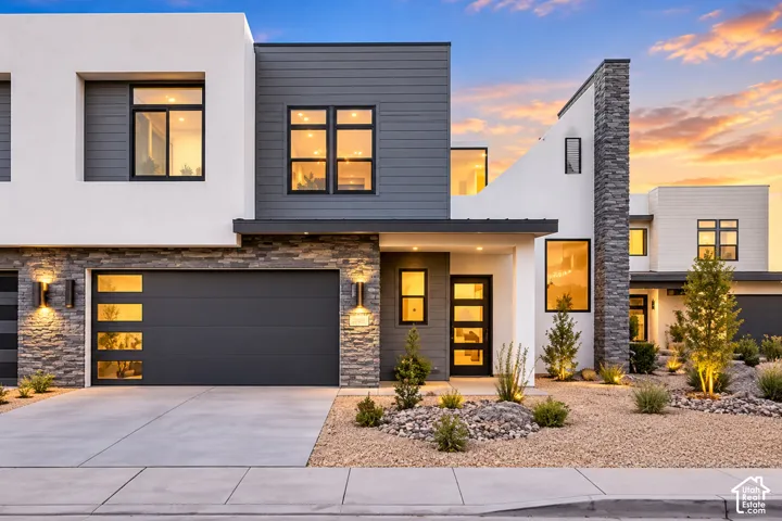 Modern architectural design with a flat roofline, stone veneer accents, an integrated garage, a concrete driveway, and xeriscape landscaping