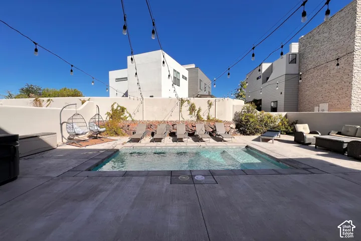 Outdoor swimming pool with integrated steps, surrounded by concrete decking, and string lighting overhead
