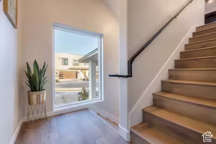 Wood-finish flooring, staircase with wood treads, black metal handrail, and a large window