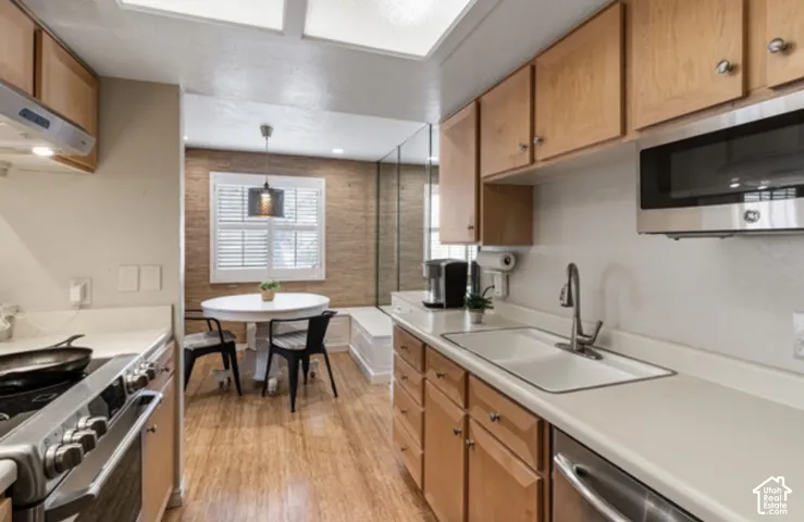 Kitchen featuring wood-finish flooring, light wood cabinetry, stainless steel appliances, and a built-in banquette