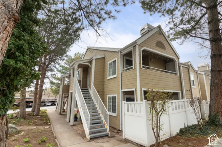 Multi-level building exterior featuring light brown siding, white trim, a white privacy fence, and multiple balconies