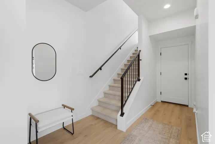 Light wood-finish flooring, white walls, and a staircase with a black metal railing