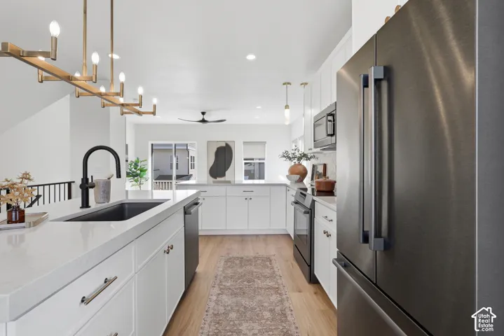 Modern kitchen featuring white cabinetry, light wood-finish flooring, a matte black sink and faucet, and sleek stainless steel appliances