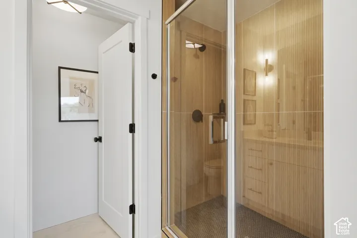 Glass-enclosed shower with dark tile flooring, a wall-mounted showerhead, and a vanity featuring built-in cabinetry and sconce lighting