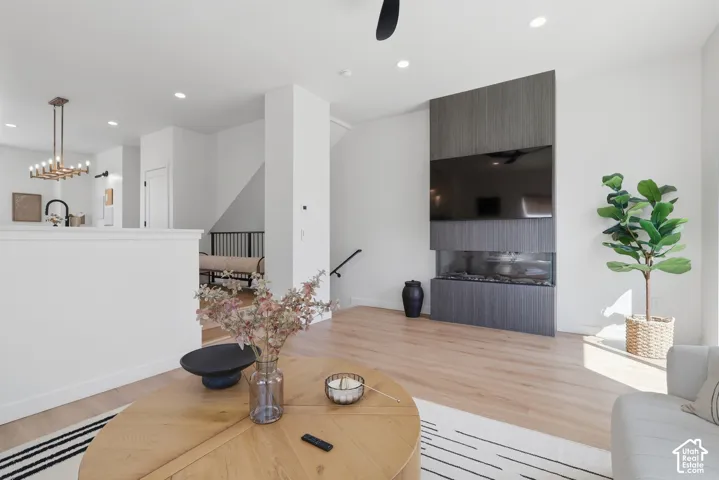 Open-concept living area featuring light wood-finish flooring, a built-in linear fireplace with a textured surround, recessed lighting, and a modern chandelier