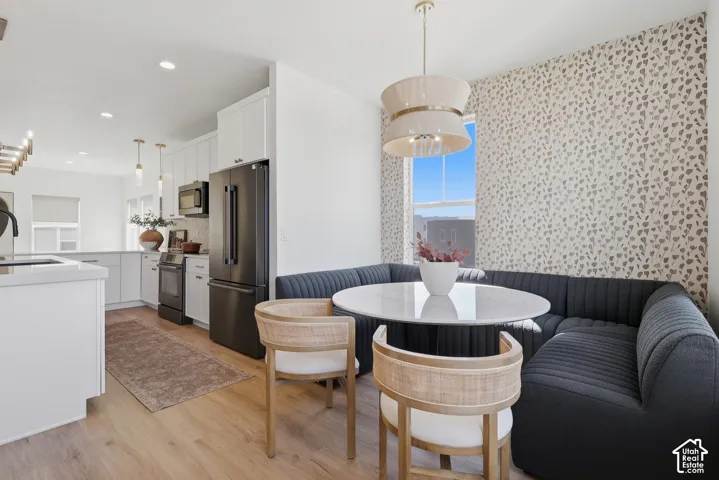 Light wood-finish flooring, white cabinetry, dark stainless steel appliances, built-in dining nook, and a decorative pendant light fixture