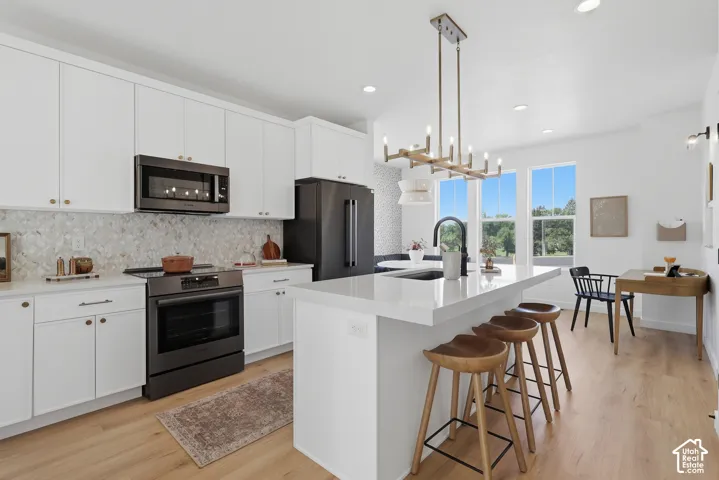 White cabinetry with gold-tone hardware, full suite of black stainless steel appliances, and a mosaic tile backsplash