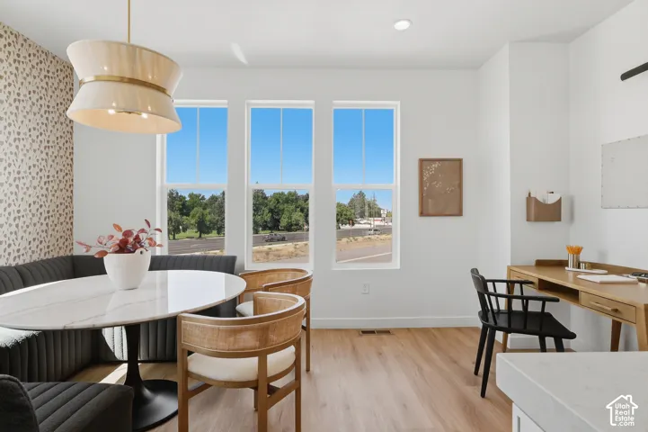 Built-in banquet seating with textured upholstery, three tall windows, wood-finish flooring, a built-in desk, and a tiered chandelier