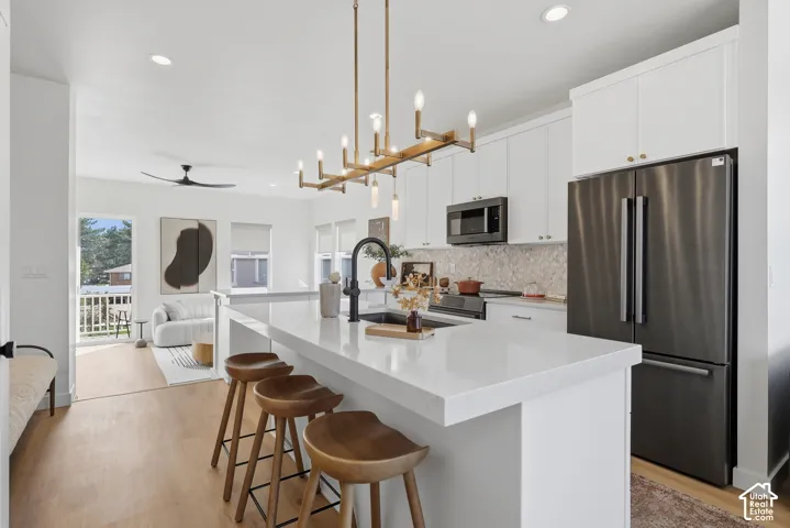 Contemporary kitchen featuring white cabinetry, a large kitchen island with counter seating, a stainless steel refrigerator, and wood-finish flooring