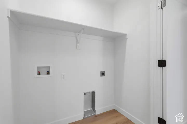 Dedicated laundry alcove featuring white walls, a built-in white shelf, and wood-finish flooring