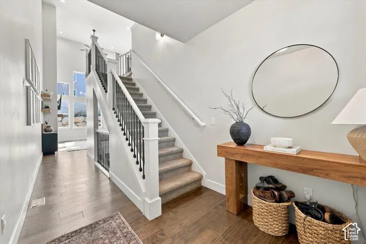 High ceilings with recessed lighting, wood-finish flooring, two-story windows, and a carpeted staircase with wrought iron balusters