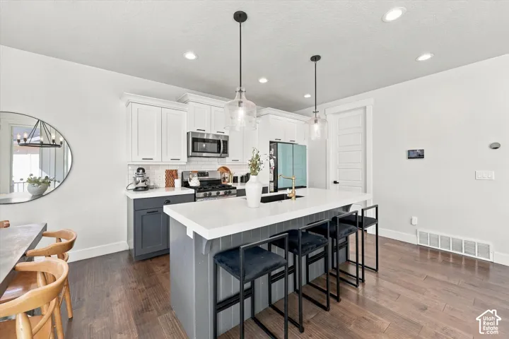 Spacious kitchen featuring an expansive island with seating, pendant lighting, stainless steel appliances, two-tone cabinetry, and wood-finish flooring