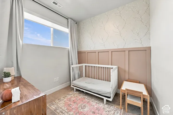 Large window with natural light, decorative accent wall with branches pattern, board and batten wainscoting, and carpeted flooring