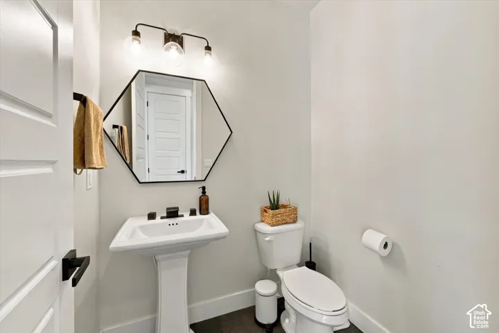 Pedestal sink with matte black faucet, hexagonal mirror, and three-light vanity fixture