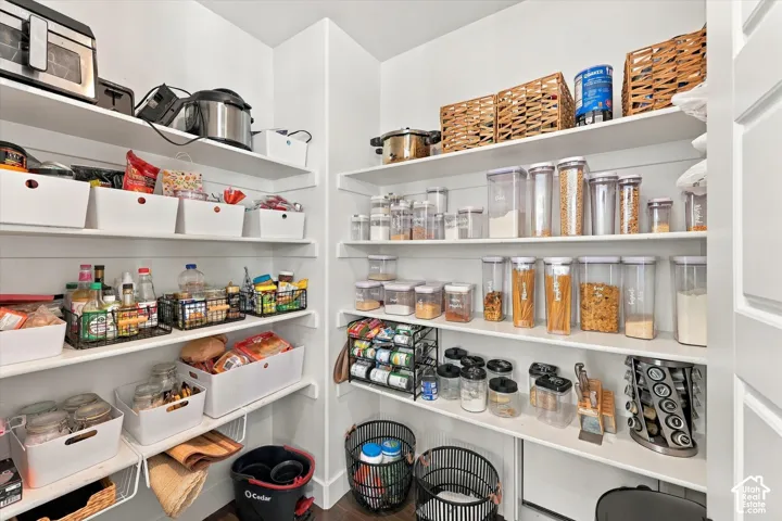 Spacious walk-in pantry with extensive built-in shelving, white wall finishes, and dark wood-finish flooring