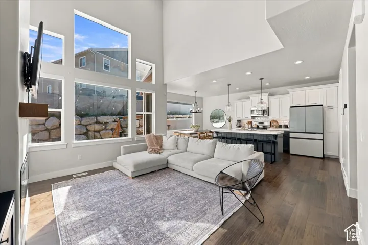 High ceilings, expansive windows, dark wood-finish flooring, white cabinetry, and a kitchen island with pendant lighting