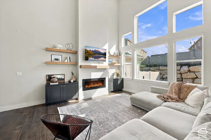 High ceilings with expansive windows, an electric fireplace, dark wood-finish flooring, and built-in shelving and cabinetry