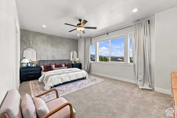 Textured accent wall, large windows with scenic backdrop, recessed lighting, ceiling fan, and light-toned carpeting