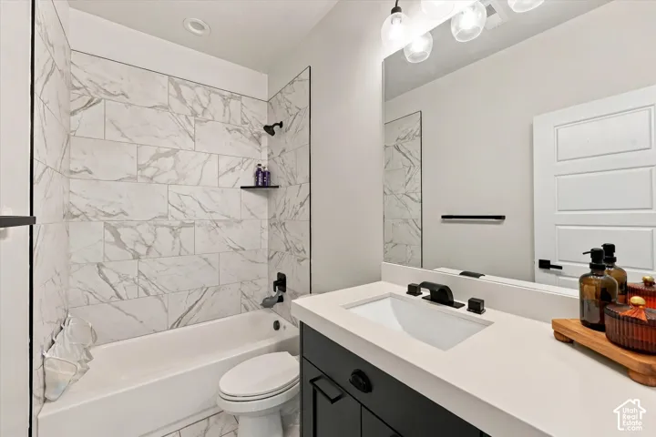 Bathtub with white subway tile surround, dark-finish fixtures, and a glass partition