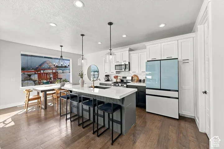 Wood-finish flooring, recessed lighting, white shaker-style cabinetry, a kitchen island with seating, and a large window