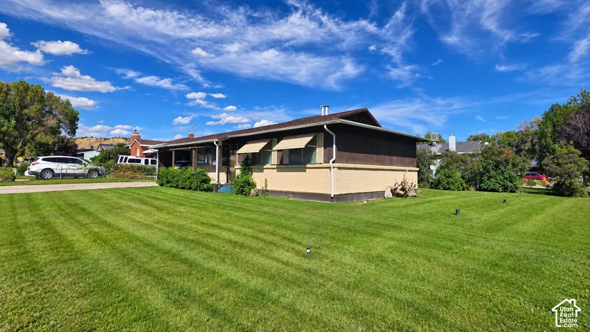 Expansive green lawn with visible mowing stripes, light-colored brick exterior, dark wood-tone siding, and multiple windows with awnings