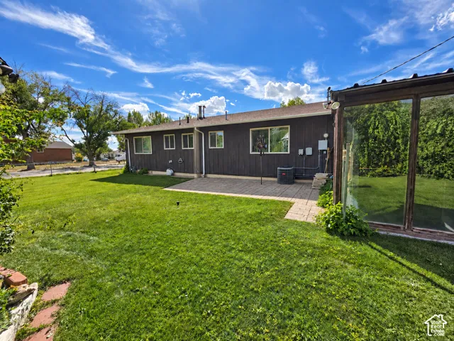 Expansive rear lawn, paved patio, and dark-stained exterior siding with white-framed windows