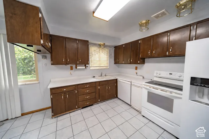 Kitchen featuring wood-finish cabinetry, white countertops, a window, white appliances, and tiled flooring