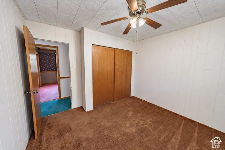 Carpeted room featuring a ceiling fan with light fixture, paneled walls, and a recessed closet with wood-finish doors