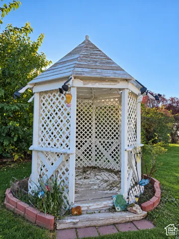 Hexagonal gazebo with lattice paneling, a peaked roof, and a perimeter brick border