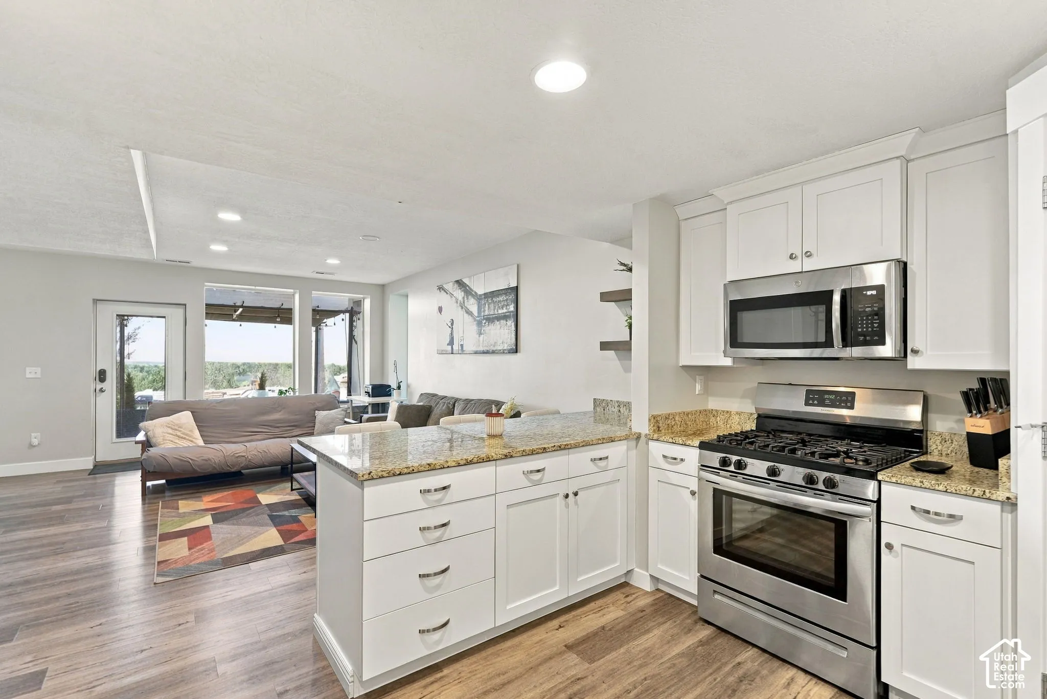 White cabinetry with granite countertops, stainless steel appliances, and wood-finish flooring