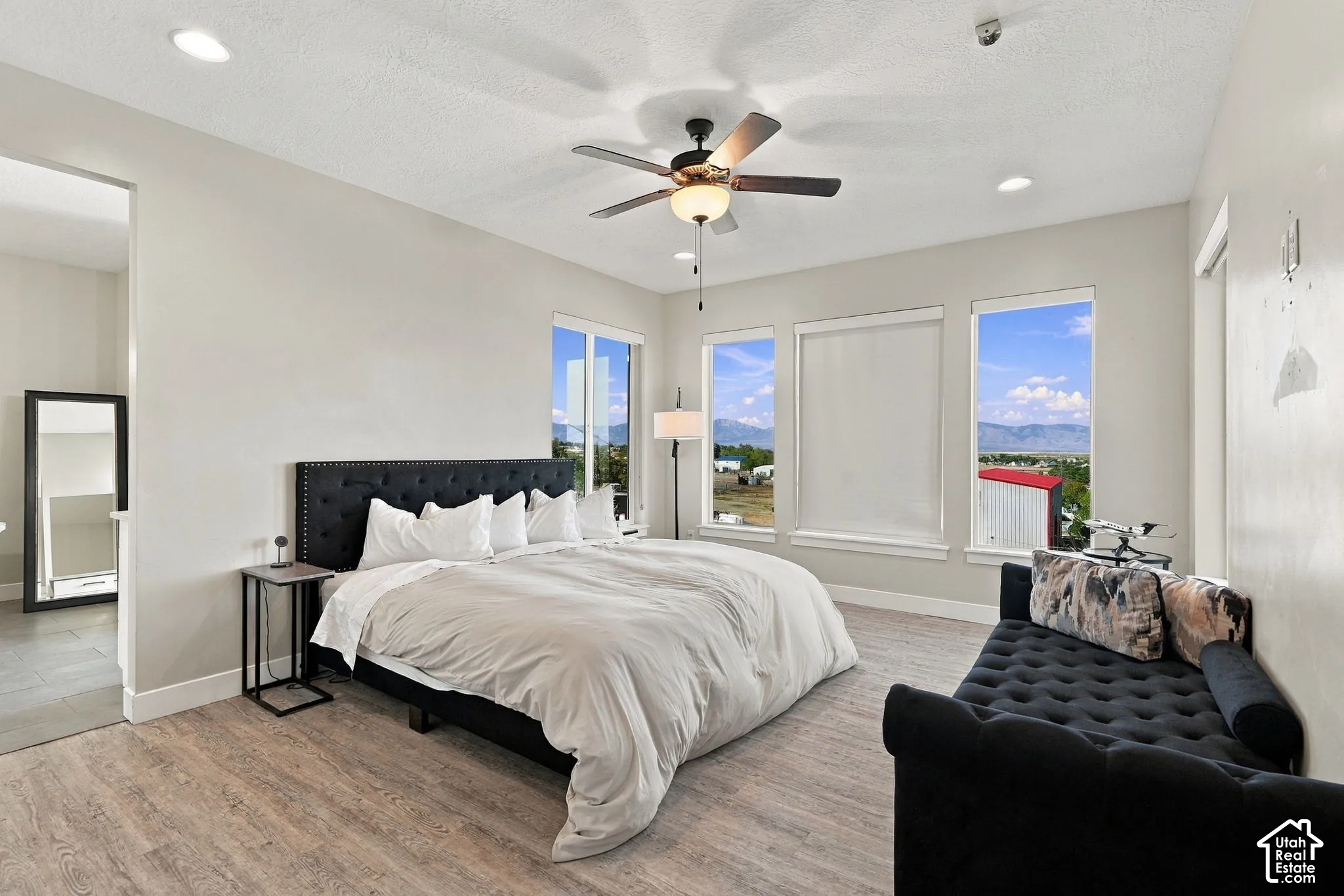 Recessed lighting, ceiling fan with integrated lighting, wood-finish flooring, multiple windows, and a tufted headboard
