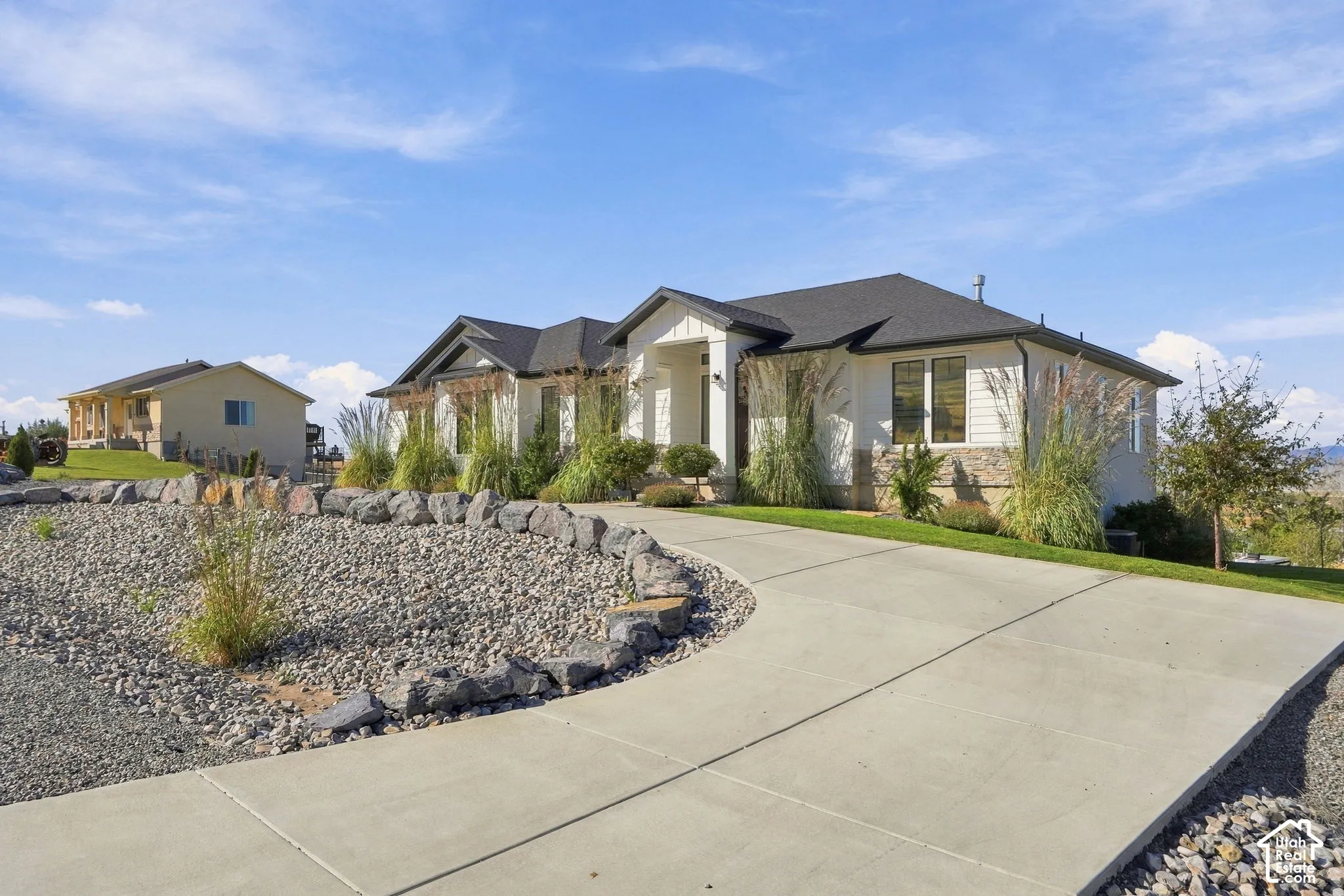 Concrete driveway with a gravel and rock border, leading to a residence featuring horizontal siding, stone accents, and a dark shingle roof