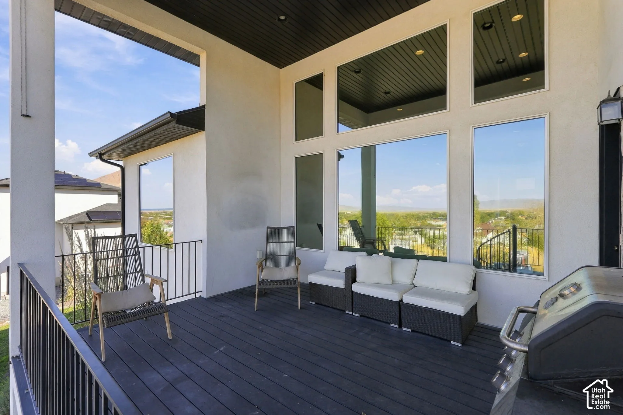 Expansive outdoor deck with dark wood-finish flooring, black metal railings, and a white stucco exterior