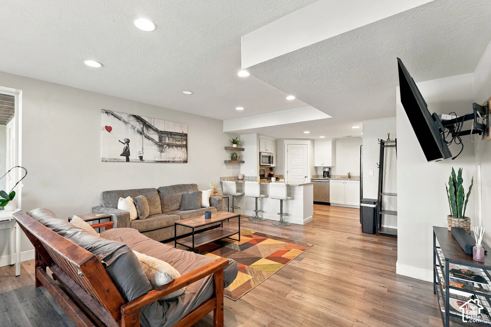 Open-concept living area featuring coffered ceiling with recessed lighting, warm wood-finish flooring throughout, and a wall-mounted flat-screen television