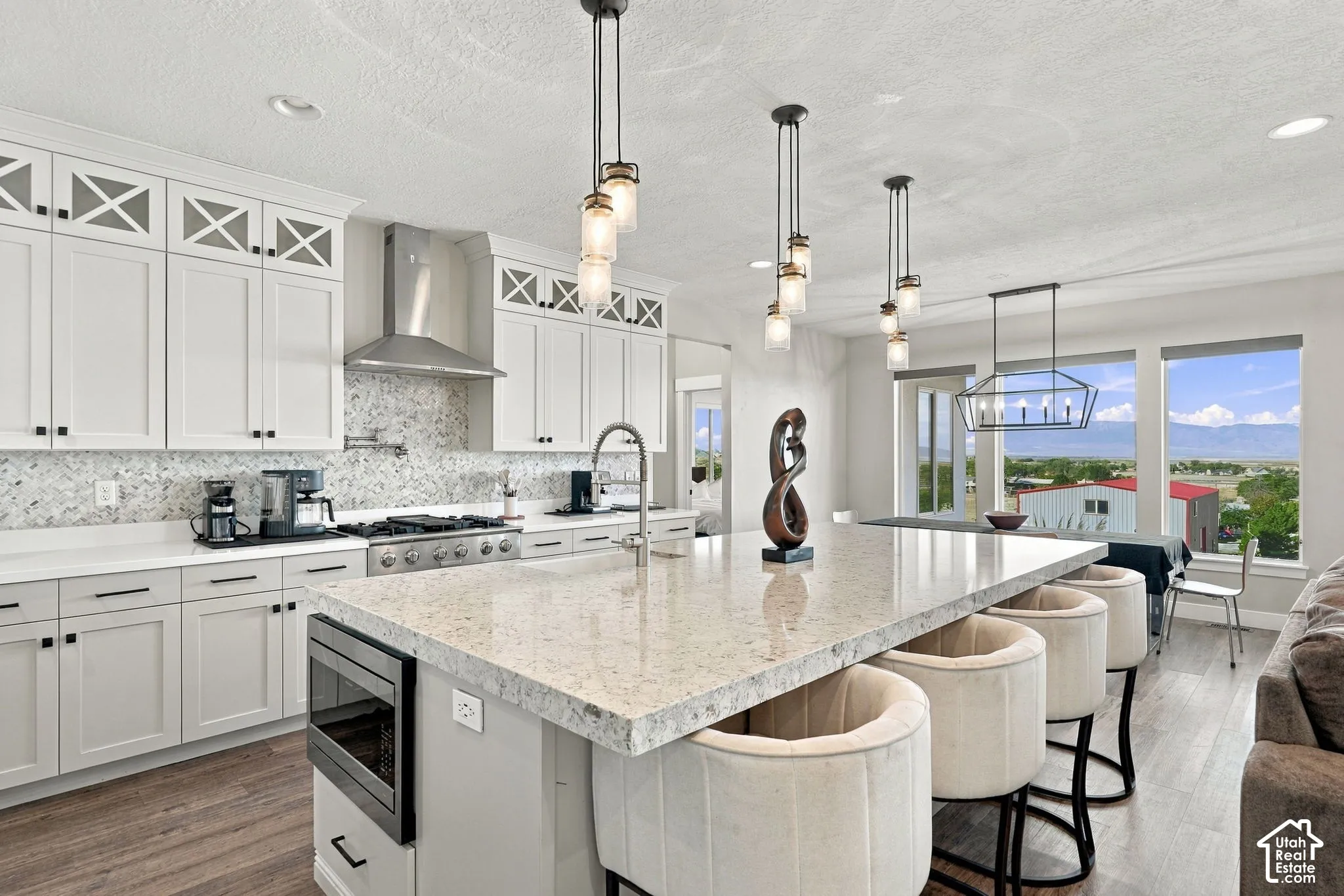 Gourmet kitchen featuring white shaker cabinetry, stainless steel range hood, stone backsplash, and a large central island with seating