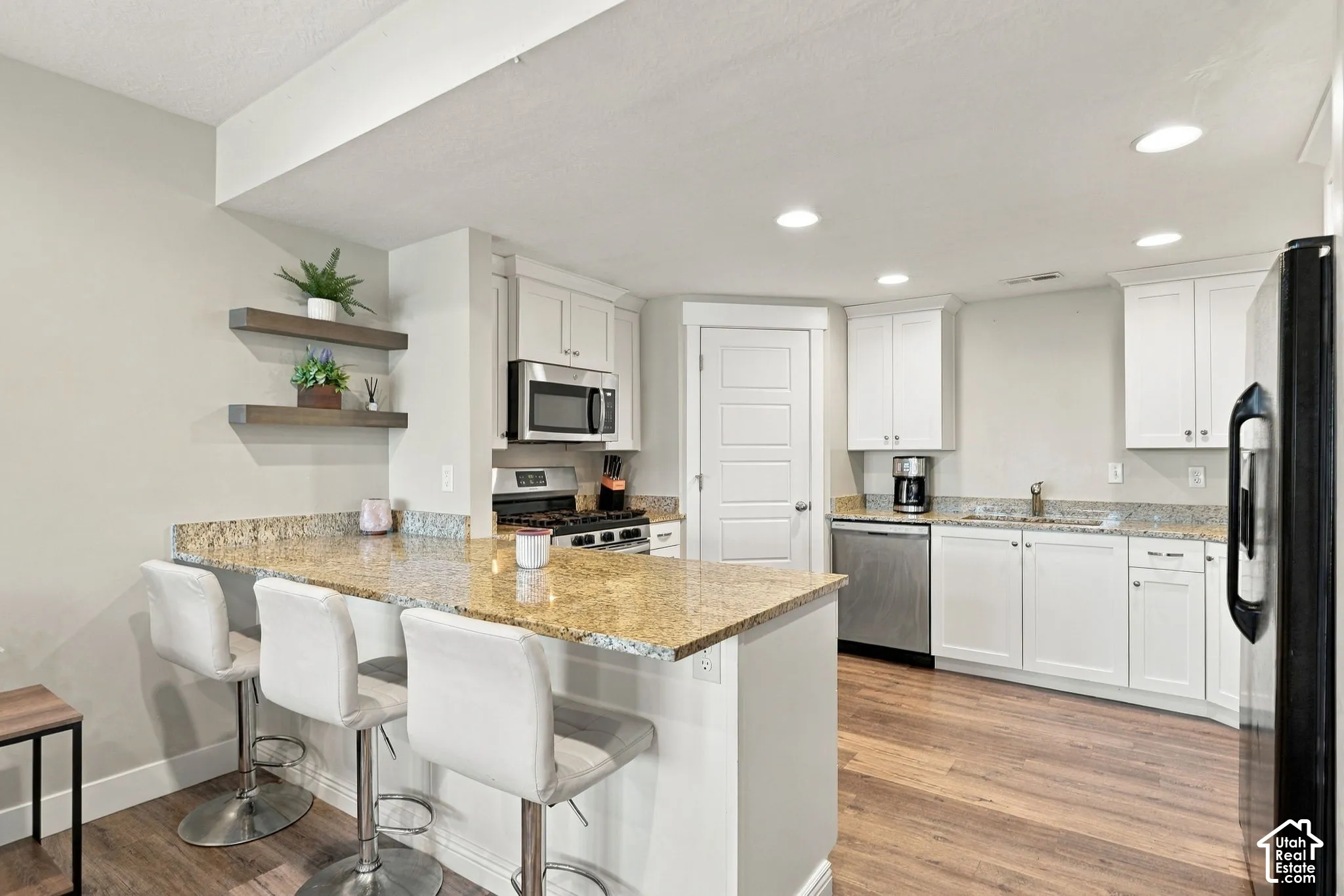 Kitchen featuring a breakfast bar with stone countertops, stainless steel appliances, white cabinetry, and wood-finish flooring