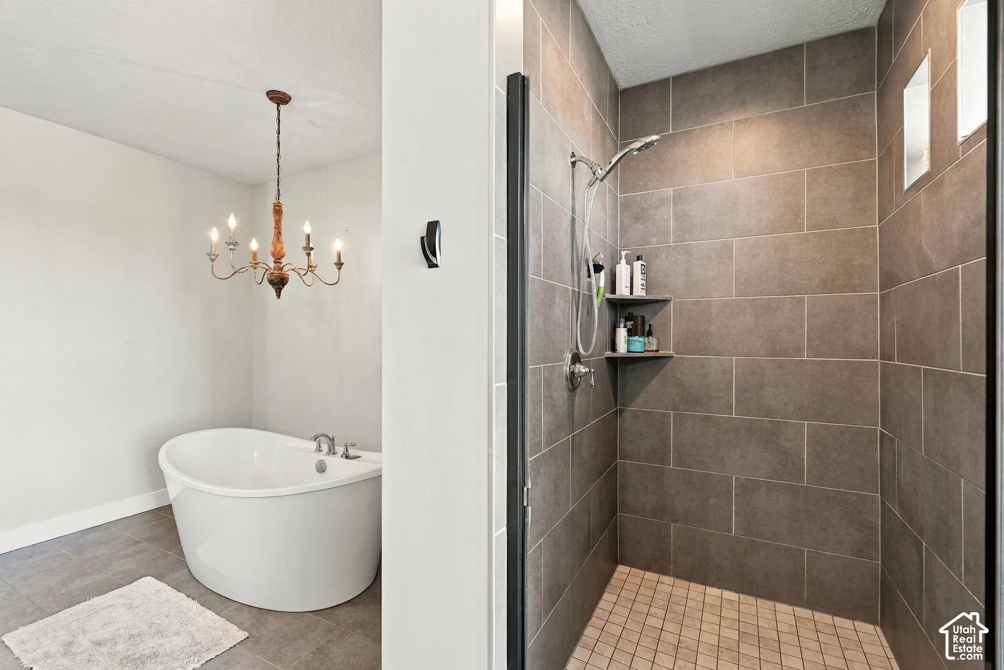 Freestanding soaking tub with chandelier and a separate shower featuring floor-to-ceiling tile, built-in shelving, and transom windows
