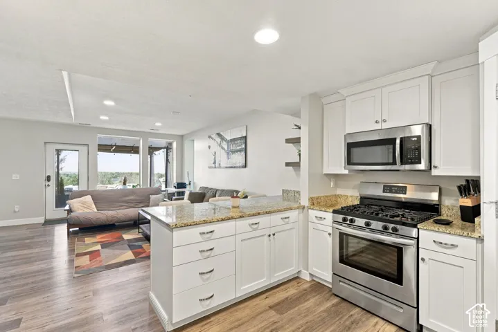 White cabinetry with granite countertops, stainless steel appliances, and wood-finish flooring