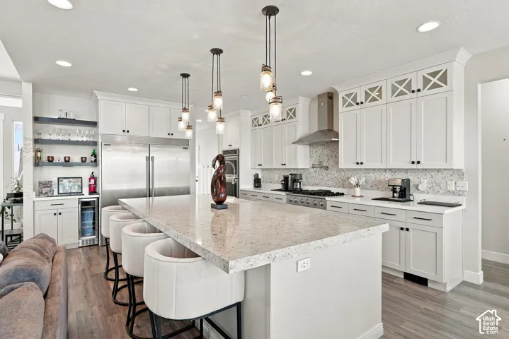 Gourmet kitchen featuring a large central island, pendant lighting, stainless steel appliances, and white cabinetry with decorative glass inserts