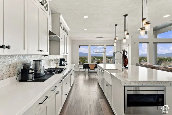 White cabinetry with black hardware, herringbone tile backsplash, wood-finish flooring, white countertops, and a built-in microwave