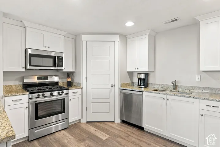 White shaker-style cabinetry, stainless steel appliances, granite countertops, and wood-finish flooring
