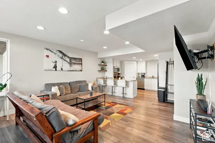 Open-concept living area featuring coffered ceiling with recessed lighting, warm wood-finish flooring throughout, and a wall-mounted flat-screen television
