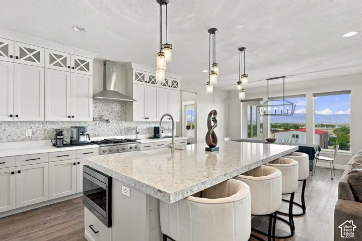 Gourmet kitchen featuring white shaker cabinetry, stainless steel range hood, stone backsplash, and a large central island with seating