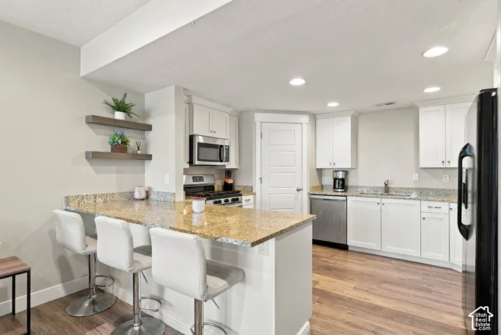 Kitchen featuring a breakfast bar with stone countertops, stainless steel appliances, white cabinetry, and wood-finish flooring