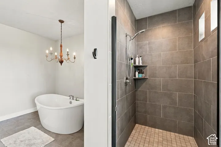 Freestanding soaking tub with chandelier and a separate shower featuring floor-to-ceiling tile, built-in shelving, and transom windows