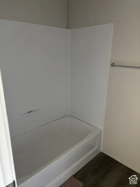 White bathtub with an integrated shower surround and wood-finish flooring