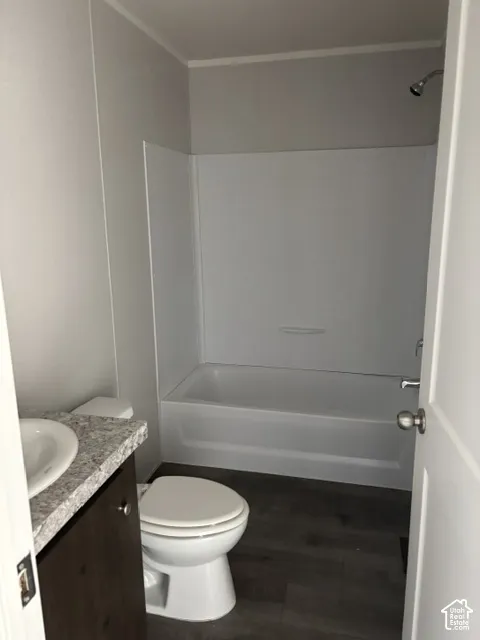 White bathtub with an integrated shower, wood-finish flooring, and a vanity with a white countertop and basin sink