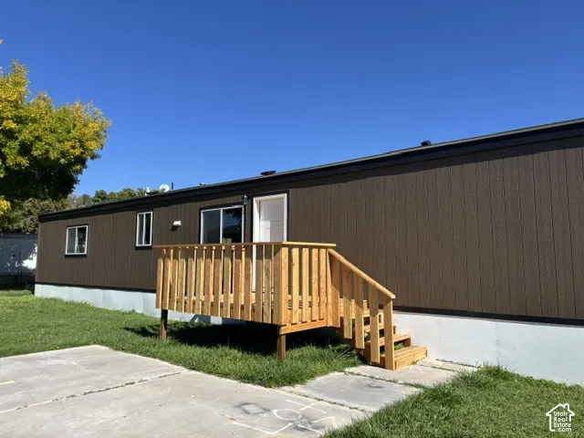 Brown vertical siding, white trim windows, white access door, wooden deck, and concrete patio