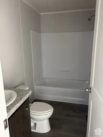 White bathtub with an integrated shower, wood-finish flooring, and a vanity with a white countertop and basin sink